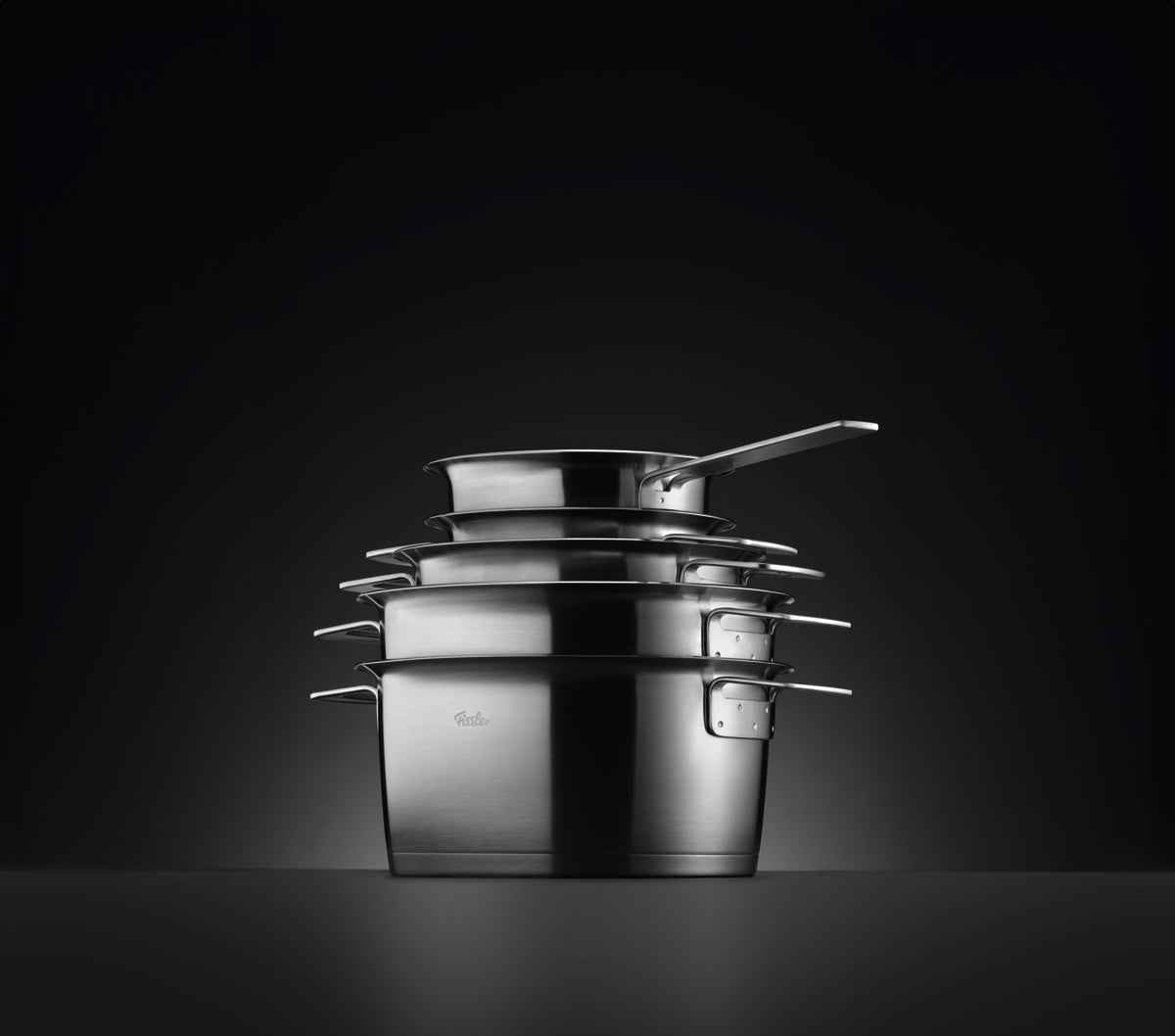 The 5-piece Cookware Set in polished stainless steel from the Fissler Phi Collection® is precise, timeless, and shown against a dark background.