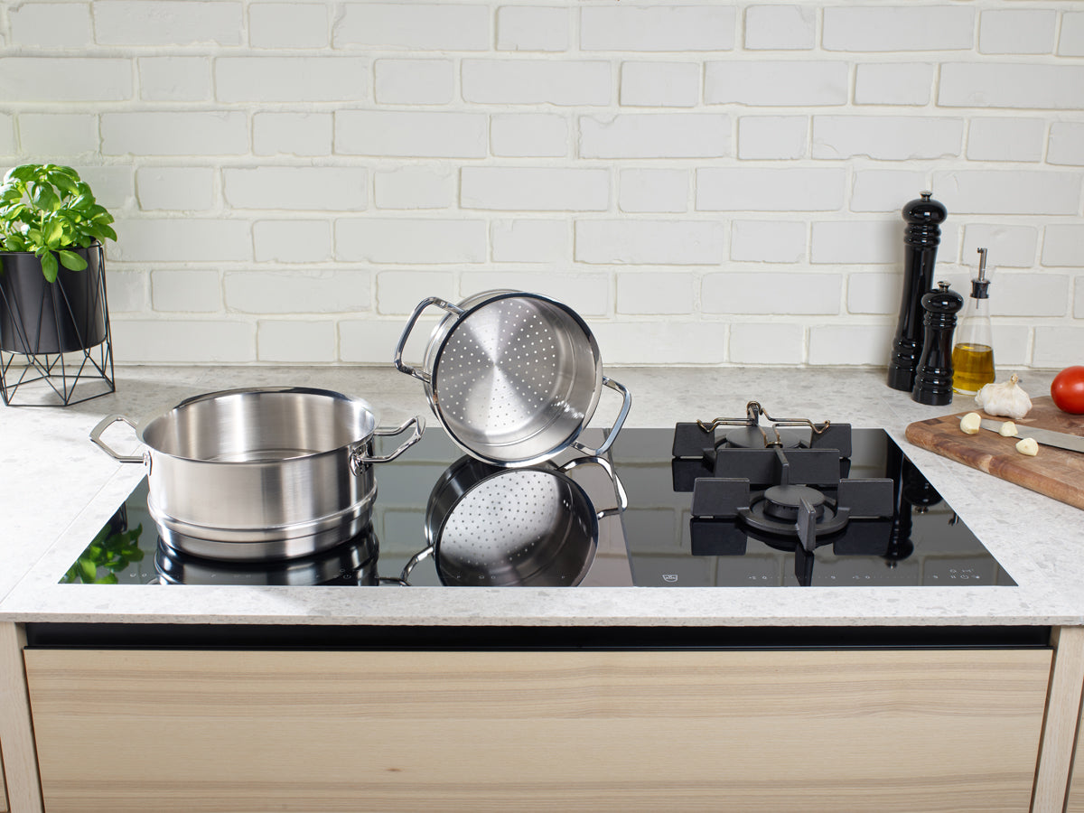 Fissler Original-Profi Collection® Cookware Set with glass lids and steamer insert on the hob, fresh ingredients, dishwasher-safe.