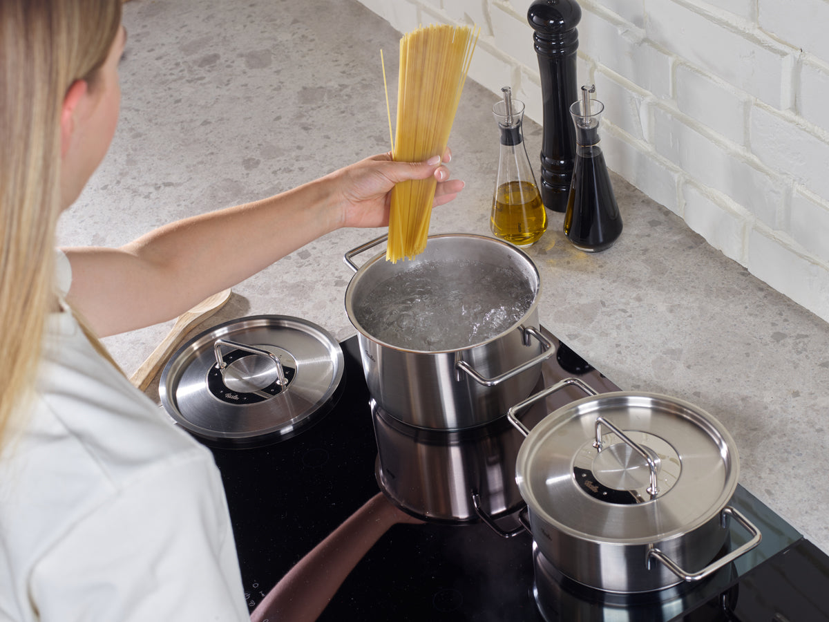 A person at the stove prepares spaghetti using pots from the Fissler Pure Collection® - high-quality German cookware for timeless home cooking.
