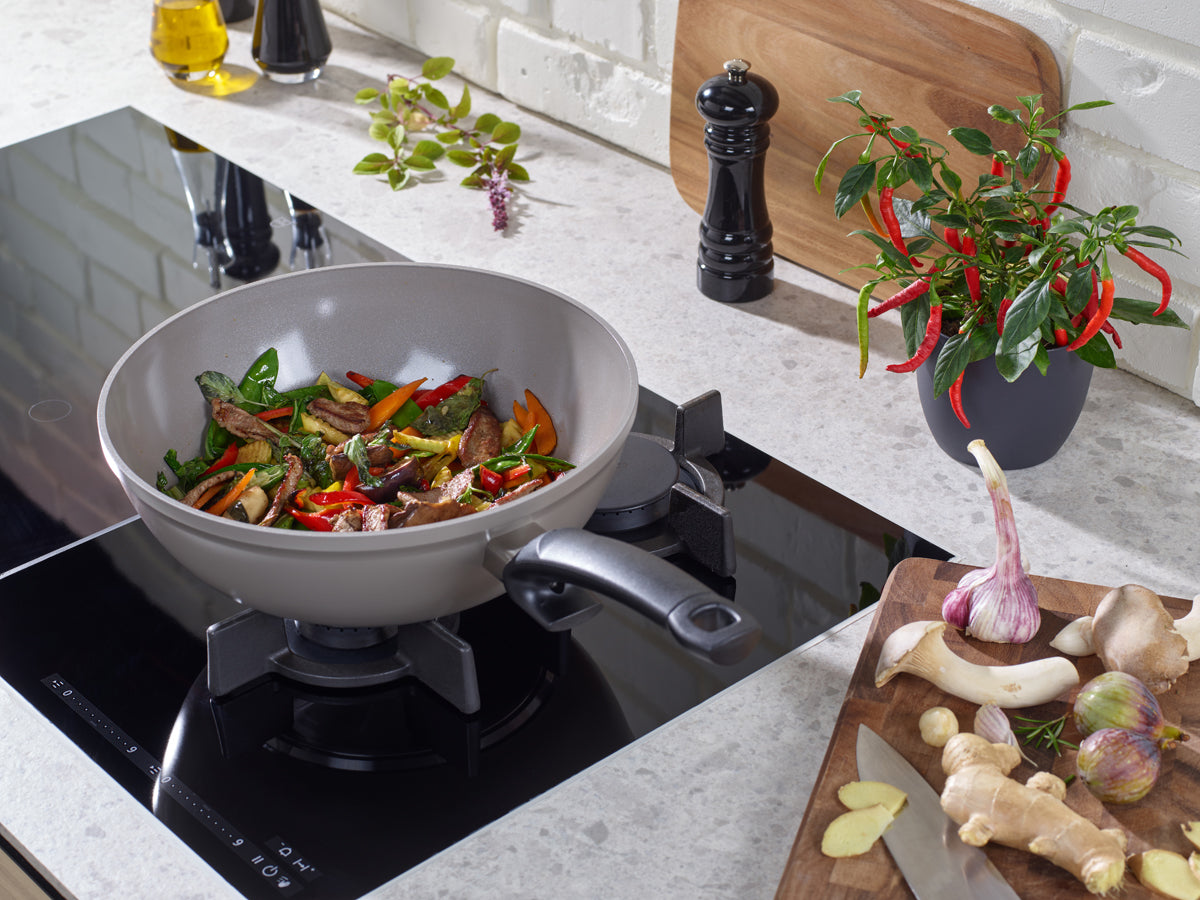 Fissler Ceratal® Wok Pan with Stir-Fry Ingredients on Stove, Herbs, Pepper Mill, Chili, Garlic & Ginger - High-Quality German Cookware.