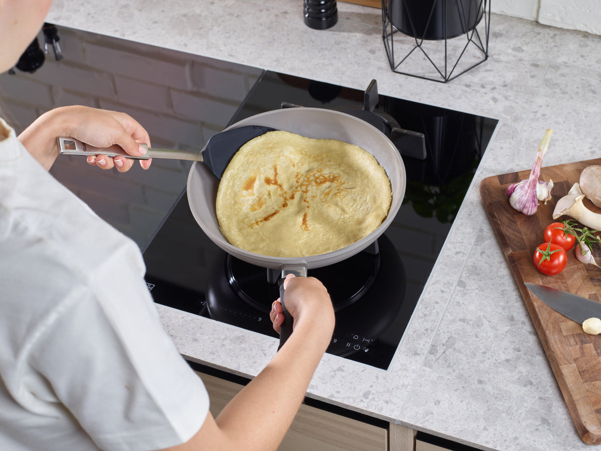 Zubereitung eines Pfannkuchens in einer Fissler-Pfanne mit dem Original-Profi Collection® Bratwender; daneben frische Produkte auf dem Schneidebrett.
