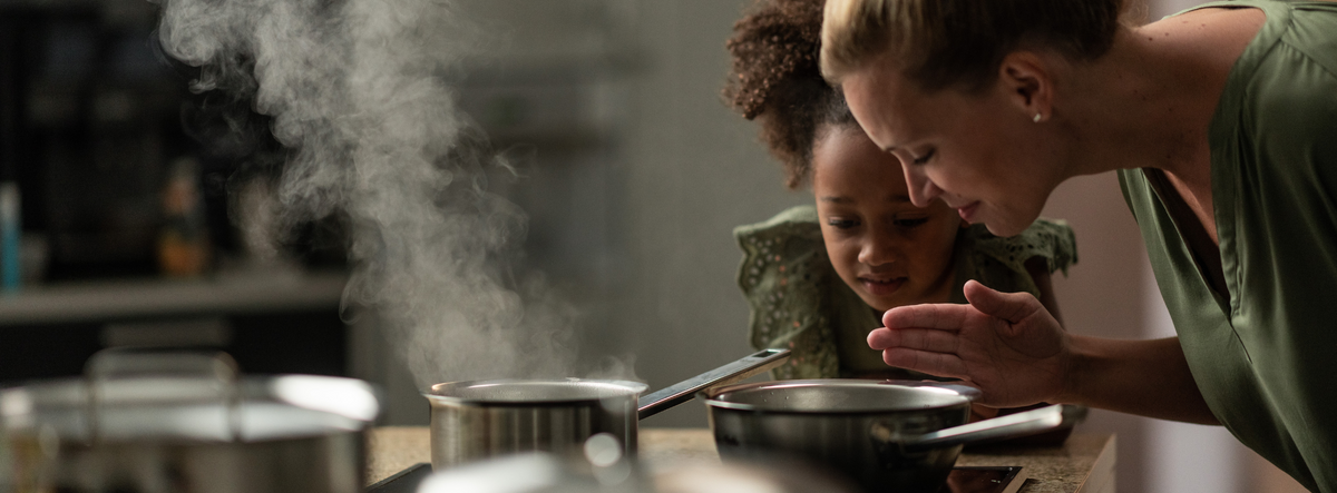 A woman and a young girl enjoy the aroma from a Fissler pot, surrounded by elegant Fissler stainless steel cookware in a modern kitchen.