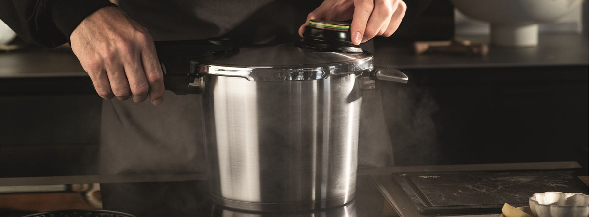 A person opens a Fissler stainless steel pressure cooker and releases steam onto a kitchen counter - German precision at work.