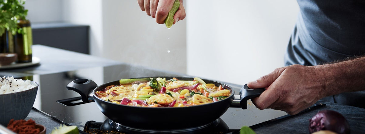 In a Fissler Frying Pan on the stove, add lime to vibrant vegetables and noodles, served with rice and fresh produce.