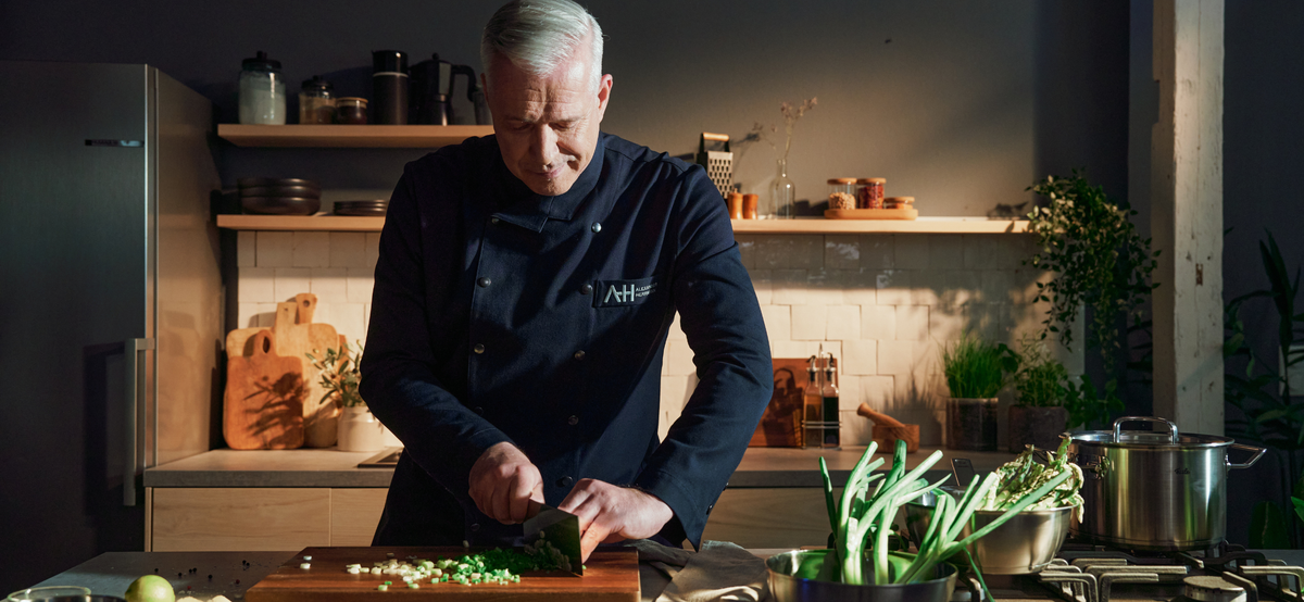 A chef cuts green onions on a wooden board in a modern kitchen, surrounded by high-quality Fissler stainless steel cookware.