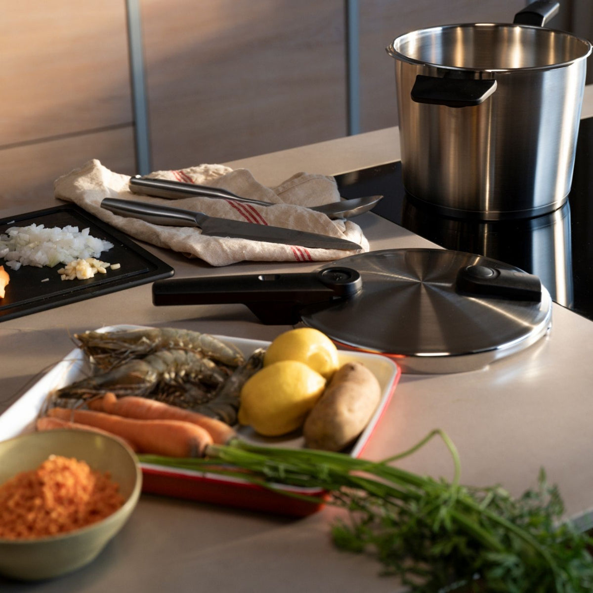 A kitchen counter with a Fissler stainless steel pot, pressure cooker lid, fresh ingredients, and utensils, ready for culinary creations.