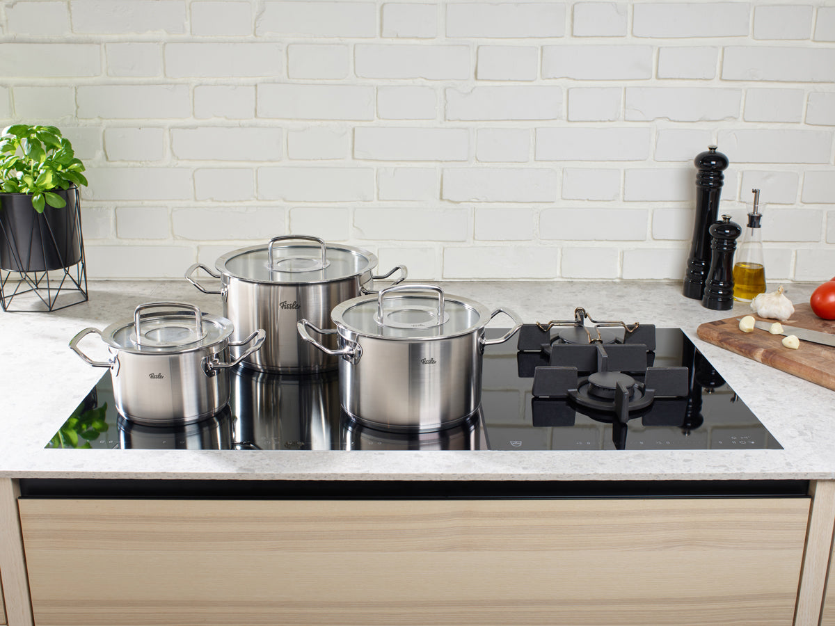 Fissler Original-Profi Collection® 5-piece Cookware Set on an elegant black hob with fresh ingredients in a modern kitchen.