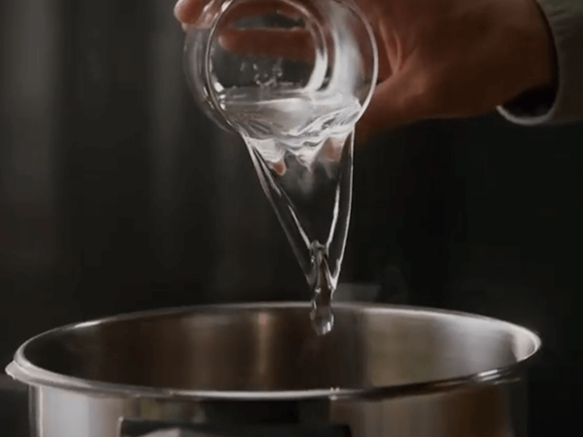Eine Hand gießt Wasser aus einem Glas in eine hochwertige Fissler-Edelstahlkanne, die deutsche Ingenieurskunst und zeitloses Design demonstriert.