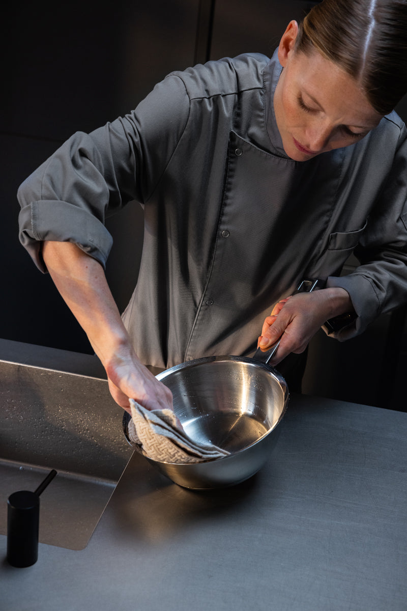 A chef in a grey uniform wipes out a Fissler Original-Profi Collection® Sauteuse 20cm, reflecting Fissler’s heritage of precision-engineered, durable German-made cookware, with a cloth in a commercial kitchen sink.