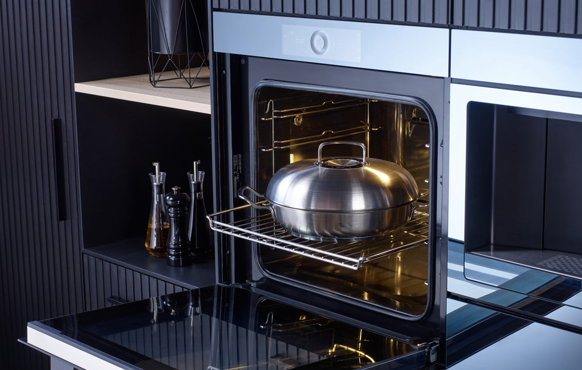 A modern oven displays a Fissler Original-Profi Collection® serving pan with Novogrill® and lid; oil bottles on the countertop.