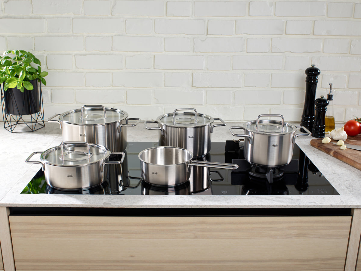 Das 5-teilige Fissler Pure Collection® Topfset glänzt auf einem schwarzen Kochfeld in einer stilvollen Küche und unterstreicht deutsche Präzision und Design.