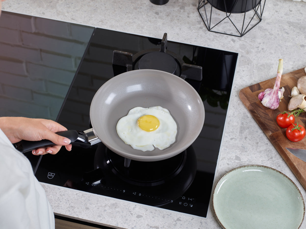 The egg cooks in a Fissler Ceratal Classic 28cm Frying Pan. Garlic, mushrooms and tomatoes nearby; the chef's precision shows.