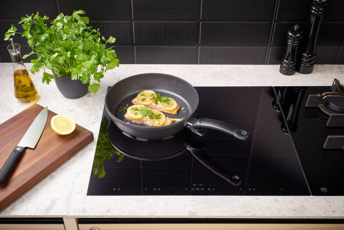 Fissler Adamant® Comfort Pfannenset (24 cm & 28 cm) auf dem Induktionskochfeld, frische Zutaten in Reichweite; deutsche Präzision seit 1845.