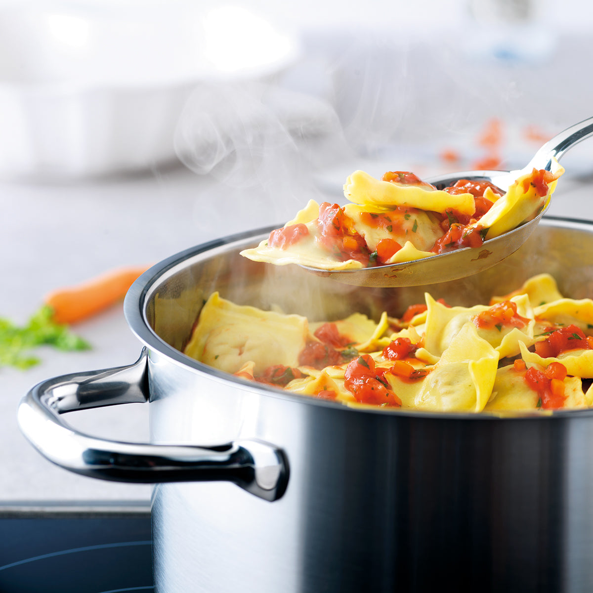 Ravioli in tomato sauce are stirred with a metal spoon in the elegant Fissler Family Line Cooking Pot, precisely made for induction cooking.