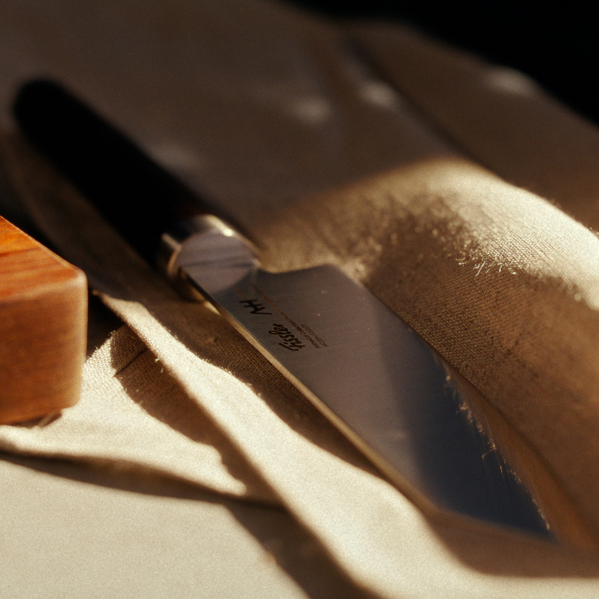 Ein präzisionsgefertigtes Fissler-Küchenmesser mit dunklem Griff auf beigem Stoff, dessen Klinge aus rostfreiem deutschem Stahl durch Sonnenlicht hervorgehoben wird.