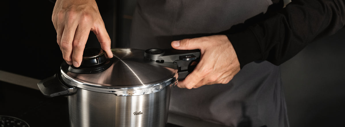 A person in a dark apron closes the lid of a Fissler stainless steel pressure cooker, highlighting German precision and craftsmanship.