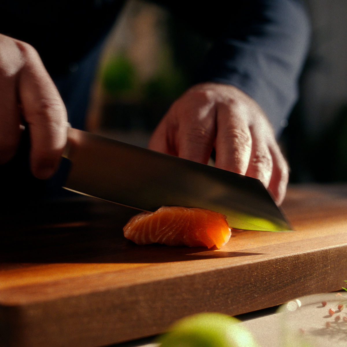 A person precisely slices raw salmon on a wooden board with a high-quality Fissler chef's knife, highlighting craftsmanship.