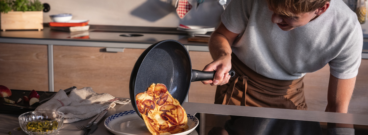 A person expertly slides a golden omelette from a Fissler Frying Pan onto a plate; premium Cookware and utensils sit on the countertop.