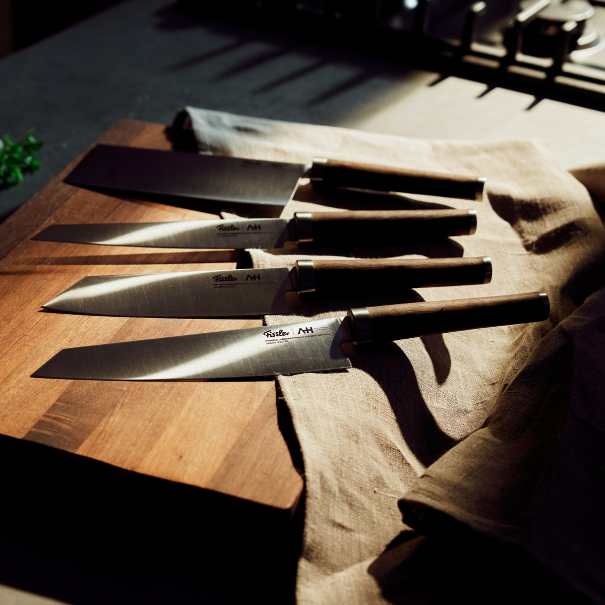 Fissler chef's knife with dark handles on a wooden board and beige cloth, sunlit in a kitchen, showing German precision and timeless design.