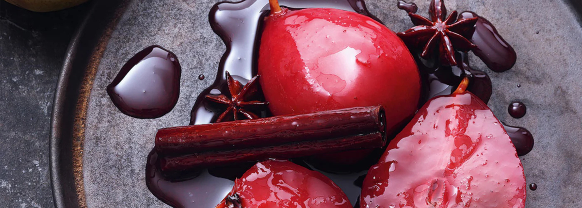 Drei pochierte Birnen in Rotwein mit Sternanis und Zimt, serviert auf einem dunklen Teller, mit reichhaltigem Sirup verfeinert - präzise angerichtet.