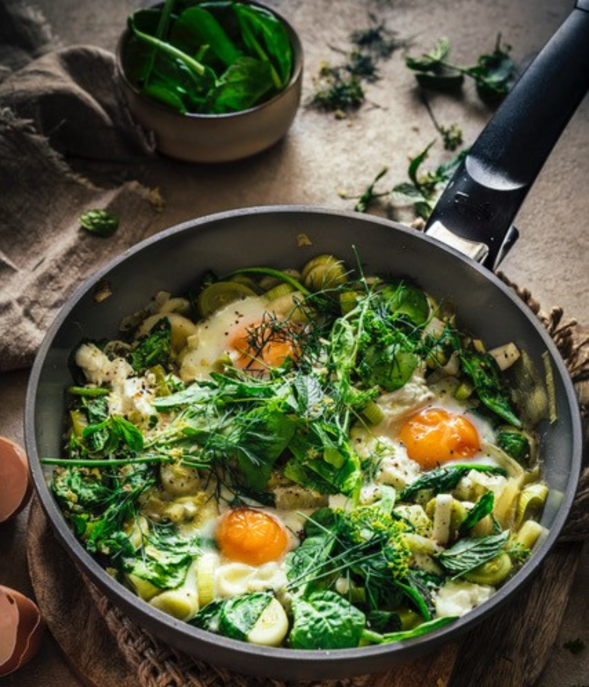 A Fissler Frying Pan with sautéed greens, herbs and three fried eggs. Fresh spinach garnishes the plate; pictured Cookware.
