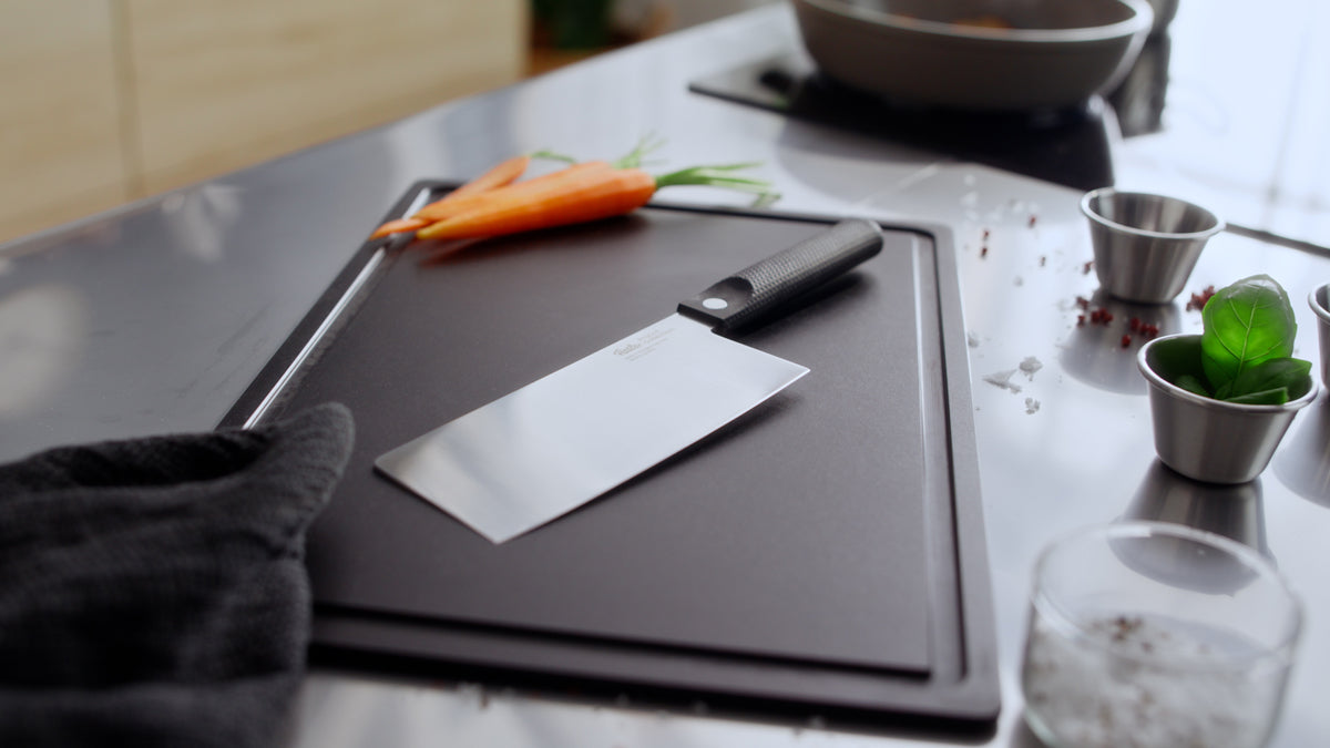 Moderne Küchenszene mit Fissler ProCut Chinesisches Kochmesser und Pfanne, die Präzision und zeitloses deutsches Design präsentieren.