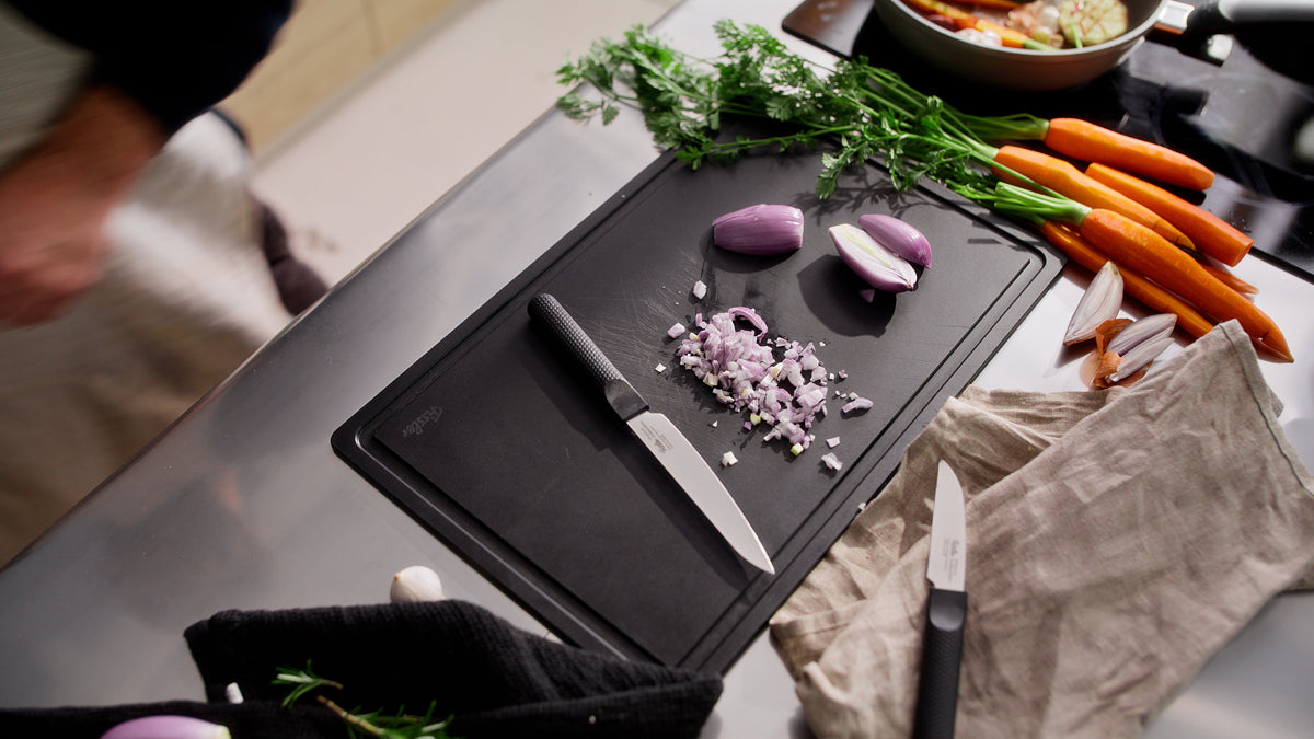 Auf einer eleganten Küchentheke ruht das Fissler ProCut Universalmesser 14cm neben frischen Zutaten auf einem schwarzen Schneidebrett.