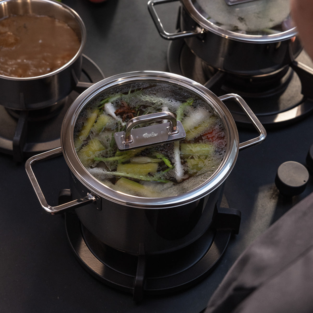 Der Fissler Viseo® Pro 20 cm pot with Glass Lid simmers on the hob; other Fissler cookware and Saucepan accompany it.
