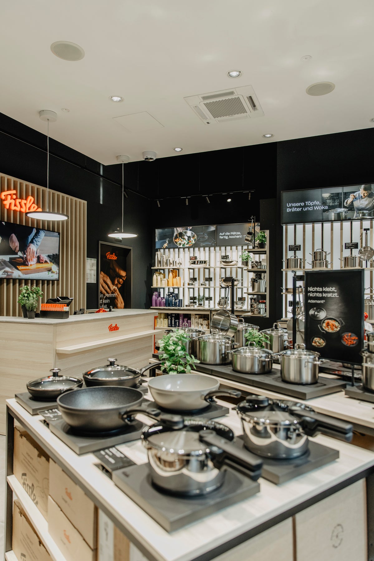 Fissler showroom interior featuring precision-engineered stainless steel pots, pans, pressure cookers, and kitchen accessories elegantly arranged on countertops and shelves. Warm lighting highlights the durability and timeless design of “Made in Germany” cookware, creating an inviting and sophisticated shopping experience.