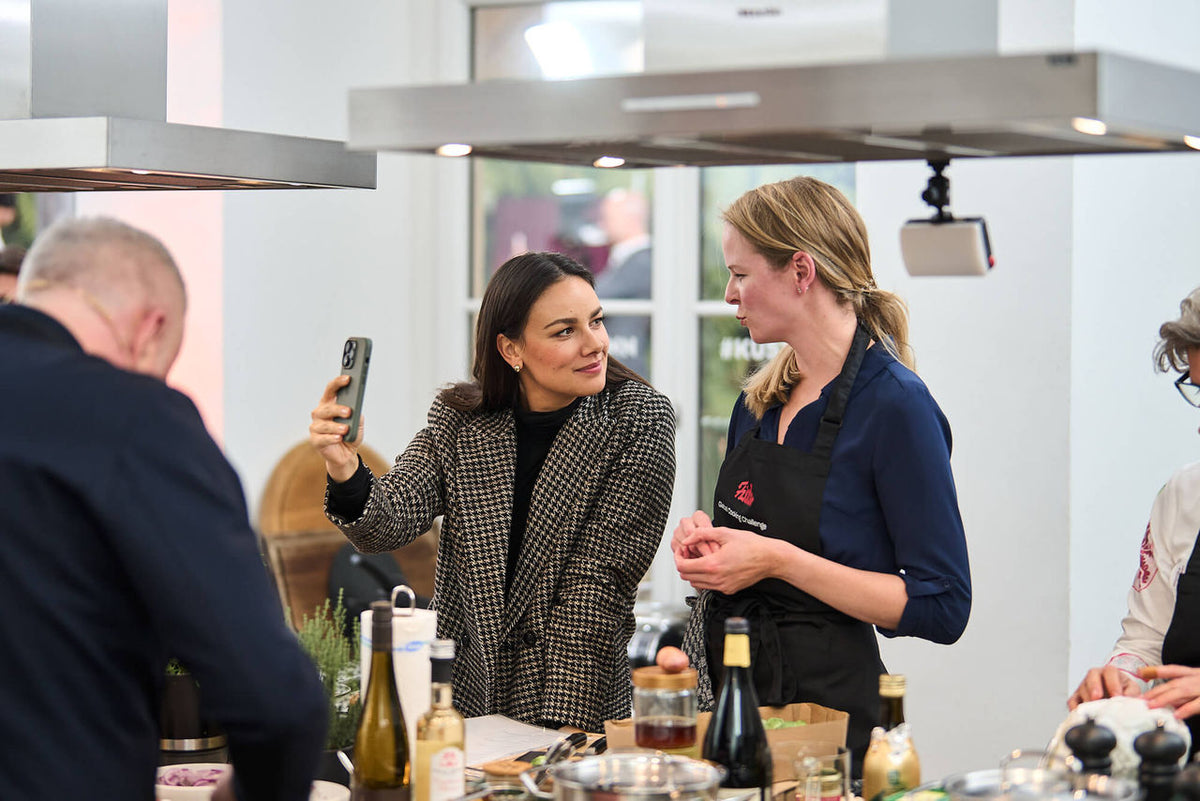 Two women in a modern kitchen with Fissler stainless steel pots and pans, smiling as they cook together with precision cookware.